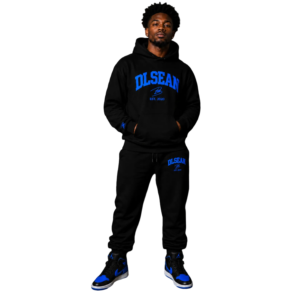 A man modeling a black two-piece sweatshirt and jogger set with blue 'DLSWAN EST. 2025' graphics, paired with blue and black sneakers, against a solid white background.